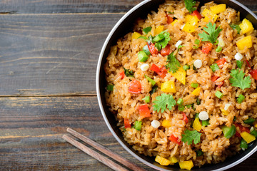 Fried rice with vegetables in cooking pan on wooden table, Asian food