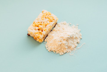 Nourishing bar and a handful of protein powder on a blue background. Delicious sports nutrition for women.