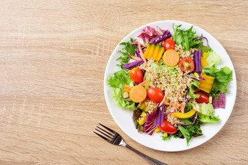 Healthy vegetables salad on white plate with fork on wooden table, top view