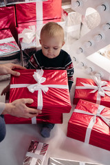 Portrait of lovely cute boy in winter patterned sweater sitting on the floor with Christmas gift wrapped in red festive paper.