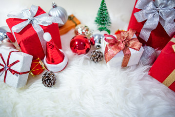 Christmas decoration on white hairy carpet. Gift box with ribbon, glossy ball, pine cone, Christmas tree and mini santa hat on fluffy rug. Present and decorative objects for New Year holiday