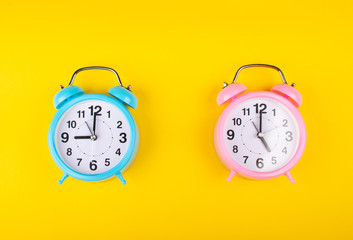 Two alarm clocks on a bright yellow background showing different time as the concept of the start...
