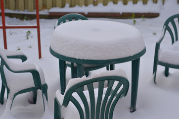 Photo of outdoor lawn furniture, table with chairs in a restaurant patio backyard completely covered in snow