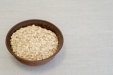 Oatmeal in a brown ceramic bowl on a linen tablecloth. The concept of cooking natural healthy food