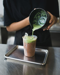 woman pouring matcha green tea into a glass of cocoa milk