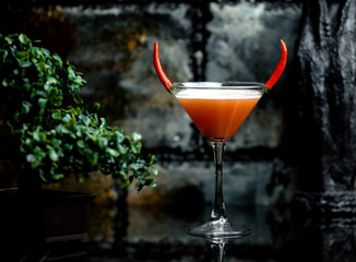 red pepper martini in martini glass garnished with two red chilis as horns