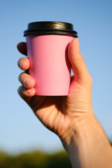 Human hand holds paper pink glass with coffee on blue background. Coffee to go, take-away coffee.