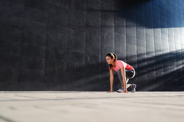 Beautiful fit caucasian brunette in sportswear kneeling and preparing to run. Back lit.
