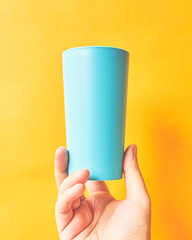 Colorful plastic cup. Plastic blue cup in hand on bright yellow background.