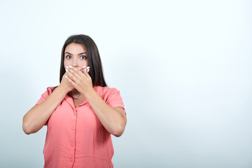 Shocked caucasian young woman in pink shirt keeping hands on mouth, looking scared isolated on white background in studio. People sincere emotions, lifestyle concept.