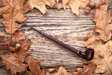 Tobacco pipe on old autumn wooden background.