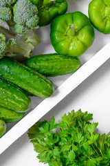 Fresh green vegetables - courgette, cucumber, paprika, parsley, broccoli on white tray and white background. Healthy snacks, vegetarian snacks concept. Organic vegetables concept