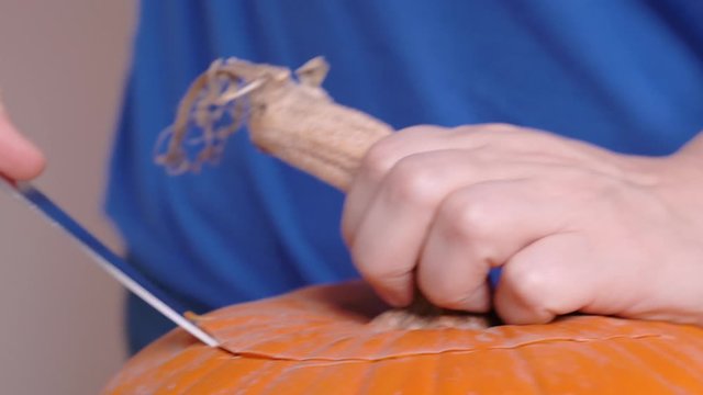 Manufacturing instructions for jack-o-lantern from the pumpkin. Halloween party preparation, hand made decoration. Woman hands, cutting the top with a pumpkin stalk by sharp knife with accuracy.
