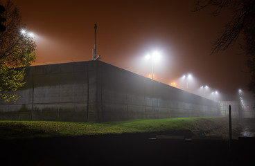Illuminated, modern prison wall on a foggy evening.