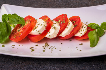 mozzarella and tomato caprese salad with basil on a white plate close-up
