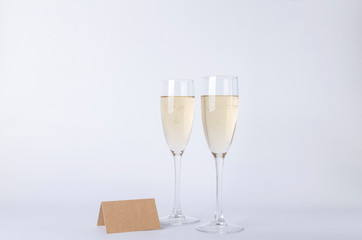 Pair of glasses full of champagne and blank place card on the gray background