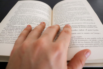 Primo piano di una mano di una donna che sfoglia le pagine di un libro, educazione e letteratura