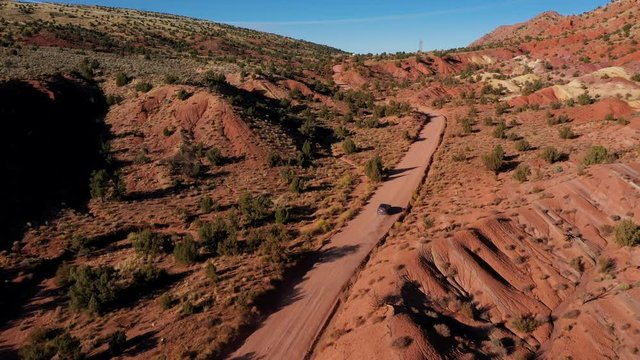 Black SUV Drive On Ground Road Crossing A Desert With Red Sand Dunes And Rocks