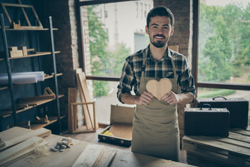 Photo of cheerful positive attractive man holding wooden heart made by himself demonstrating his...