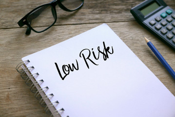 Glasses,calculator,pencil and notebook written with Low Risk on wooden background.