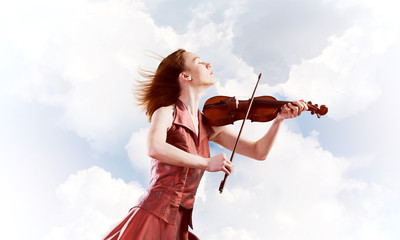 Woman violinist in red dress playing melody against cloudy sky