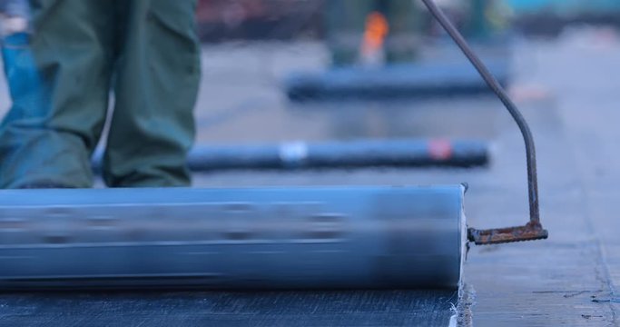 The workers heats the roll of ruberoid with the flame of a gas burner and firmly connect with a surface of stadium main field that needs to be isolated from water