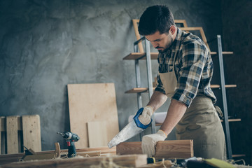 Side profile photo of serious confident focused man cutting off unneeded pieces of wooden block using saw