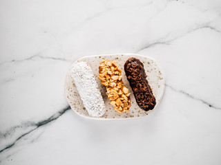 Set of three homemade eclairs on marble background. Close up view of delicious healthy profitroles with different decor elements - chocolate, peanut and sherdded coconut. Vertical.