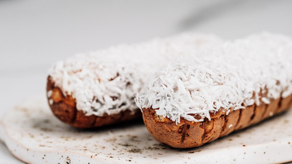 Homemade eclairs with coconut on white marble background. Close up view of delicious healthy profitroles with shredded coconut. Banner