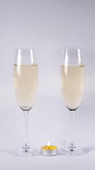 Burning candle near glasses of champagne, on a white background
