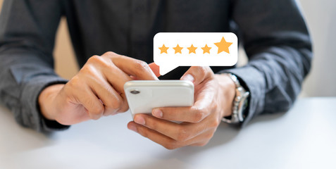 close up on businessman hand press on smartphone screen with gold five star rating feedback icon...