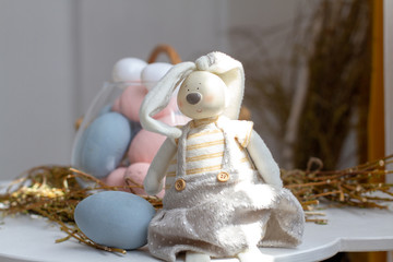 Easter bunny sits near a basket with pastel flowers Easter eggs. Religious spring holiday.