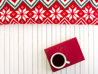 Red book and white cup of coffee on the white wooden background with autumn, winter accesories. Leisure time with book, drinking coffe