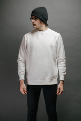 Man wearing white sweatshirt and a black hat standing over gray background. Sweatshirt or hoodie for mock up, logo designs or design prints with free space.