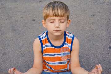 A boy is meditating sitting on the asphalt in the middle of the road.