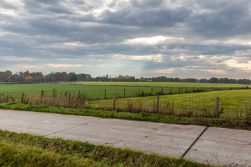 Fototapeta na wymiar Bicycle lane between farmland with fences and trees in the background, autumn day on a cloudy day in south Limburg, the Netherlands Holland