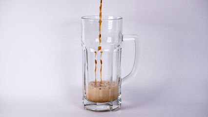 Pour beer into a glass with dark beer and foam on a white background