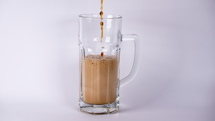 Pour beer into a glass with dark beer and foam on a white background