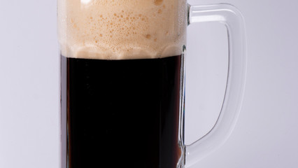 Beer glass with dark beer and foam on a white background