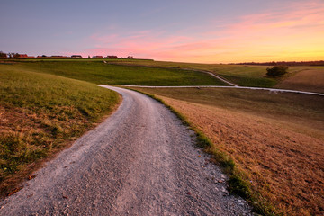 Beautiful countrsyside landscape during sunset with a dimishing gravel road and some houses on the horizon. Seen in late summer in Franconia / Bavaria, Germany near Kalchereuth