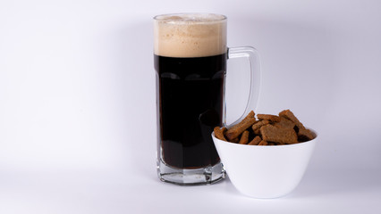 Beer glass with dark beer and crackers on a white background