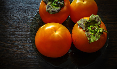 On the brown table in a plate of glass lies a juicy ripe orange persimmon