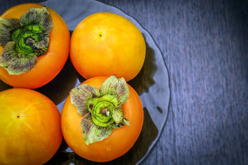 On the table is a glass plate with fresh juicy persimmons