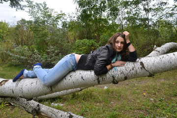 Beautiful young girl in leather jacket sleeping on a big log in the forest 