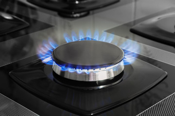 Detail of a gas stove made of black tempered glass with an open gas flame.
