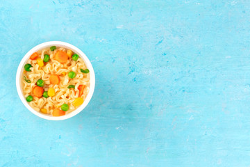 Ramen cup, instant noodles in a plastic cup, shot from the top on a blue background with copy space