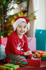 Excited little boy with a Christmas gift under fir tree at home. Portrait of happy kid in Christmas morning.