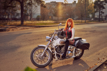 Plakat motorcycle cruiser and woman biker on the road in the autumn city at sunset