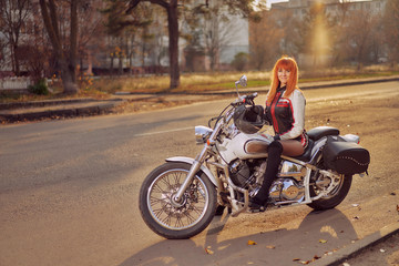 Obraz premium white motorcycle tourer and woman biker on the road in the autumn city at sunset