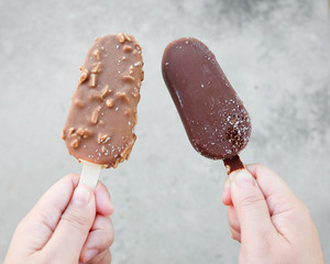 Hands holding vanilla icecreams covered with chocolate and almonds